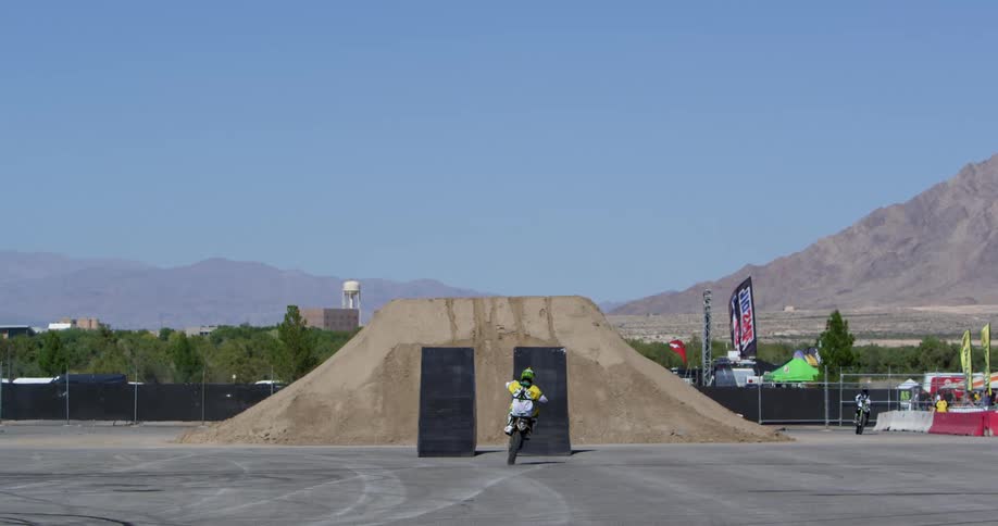 Motorcyclists take turns jumping from a ramp in a parking lot near a canyon