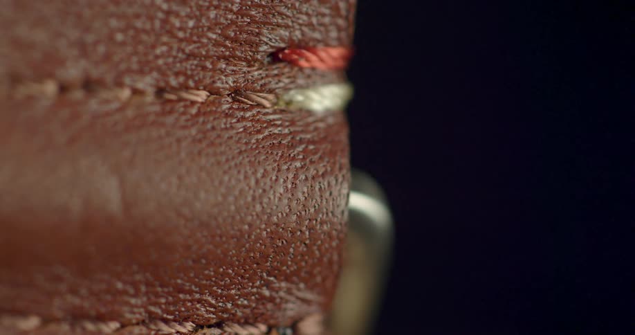 Brown leather with thread stitched into it against a black background