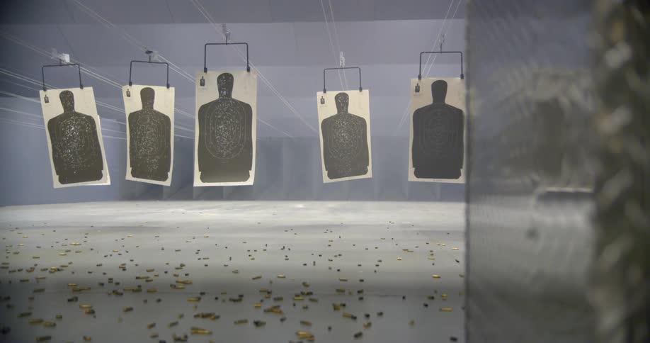 Paper targets in a shooting range shake as they hang from the ceiling and bullet casing bounce along the ground
