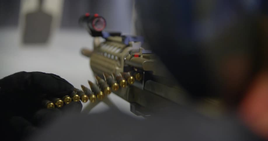 A man feeds bullets into an assault rifle while shooting at a gun range