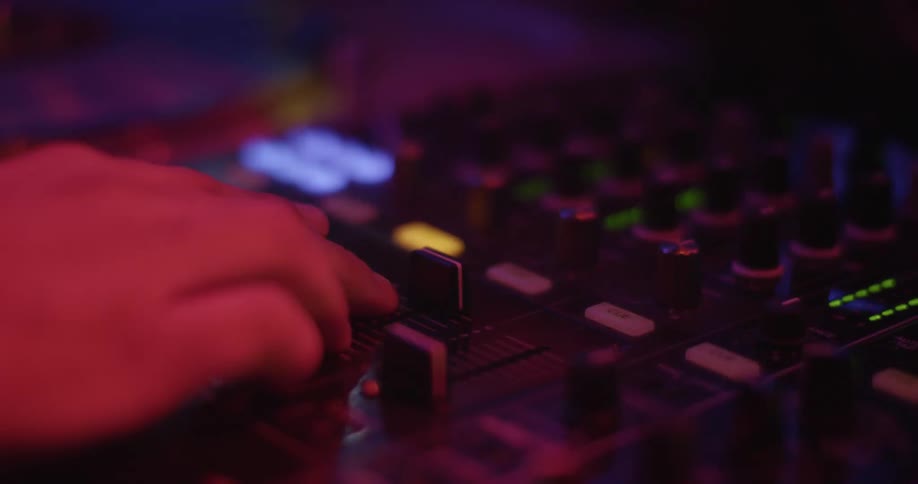 A dj turns a switch while playing in a club under flashing lights