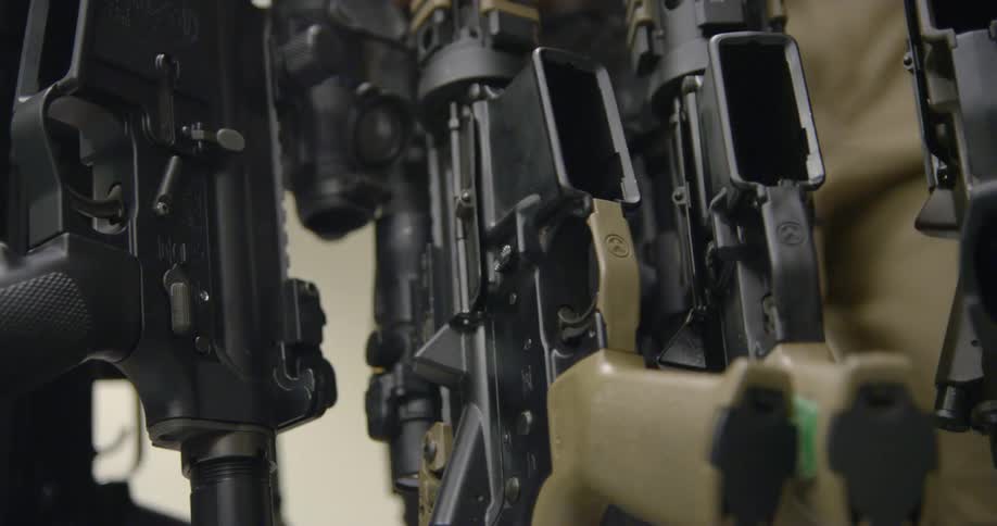 A soldier walks past a gun rack filled with rifles