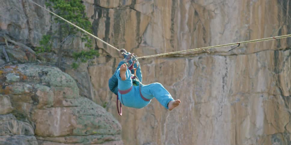 A person crosses a canyon via rope harness