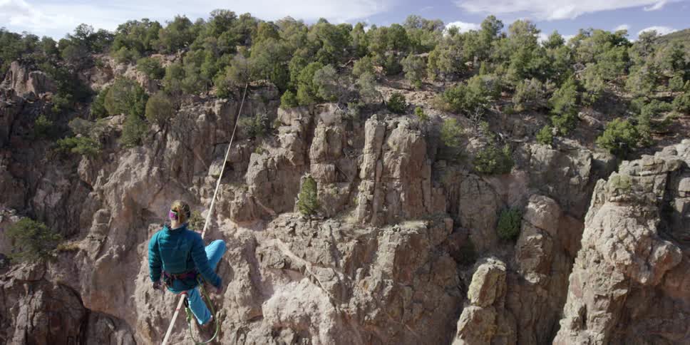 A woman sits balanced on a rope over a gorge