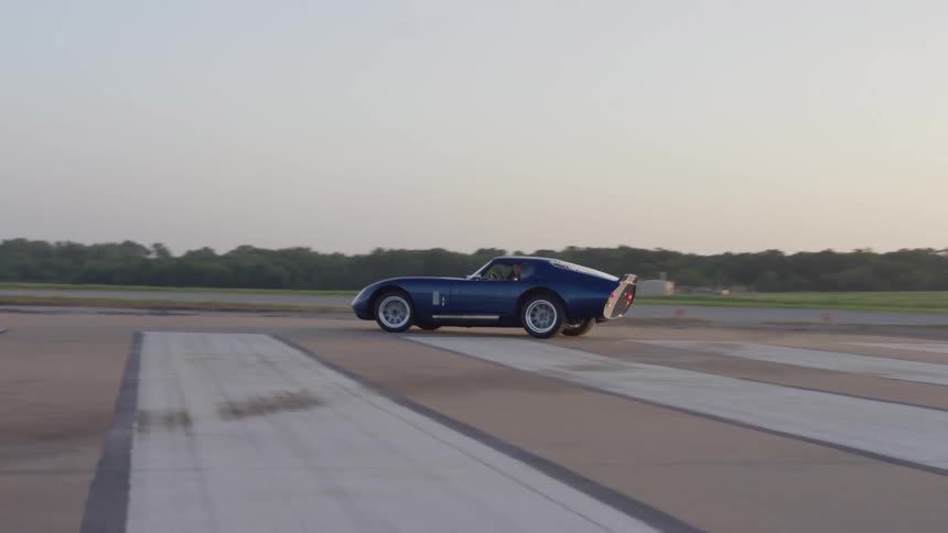 A sports car performs a uturn on an airstrip in a grassland in the evening