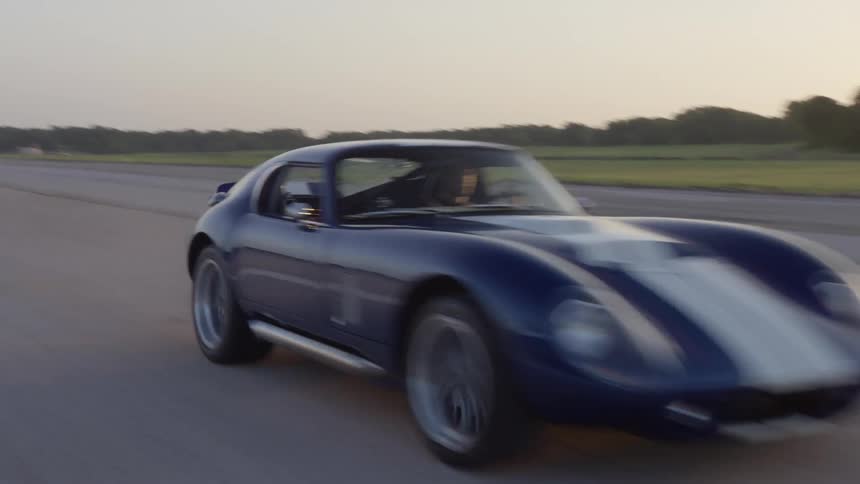 A sports car speeds down a runway in a grassland in the evening
