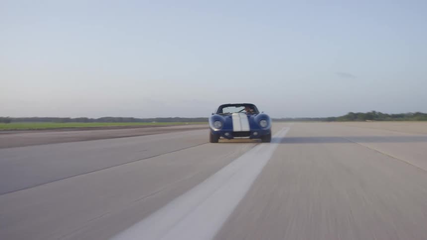 A blue sports car with a white stripe drives down a road with a white painted line in the middle during the day