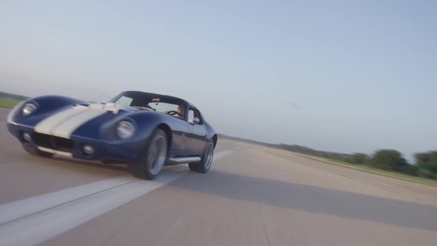 Man drives a blue coupe sports car on a paved road at day