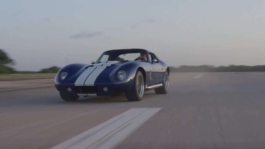 A sports car races across a racetrack during dusk