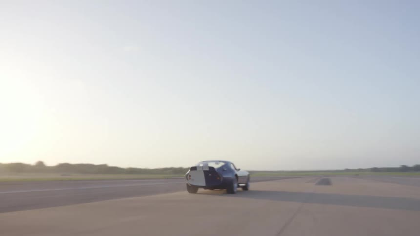 Blue coupe sports car driving down a road through the fields at sunset