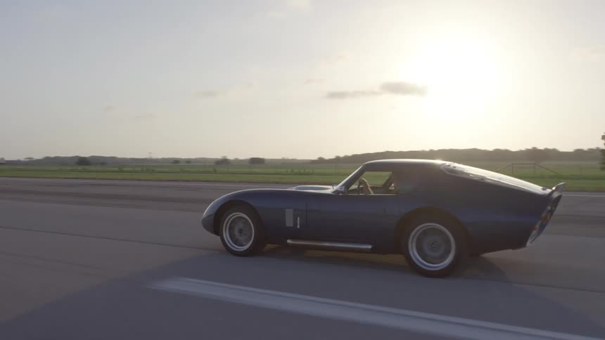 Shelby daytona coupe sports car driving on a runway at sunset
