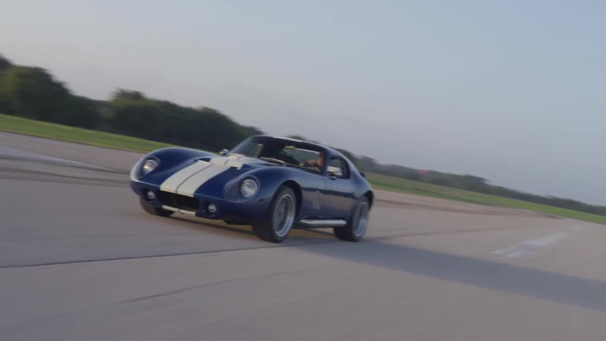 A blue sports car with a white stripe drives down a road during the day