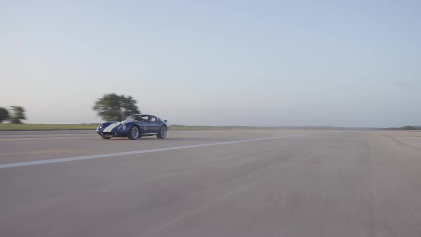 Sports car with racing strip speeds along highway past forest as sun shines from horizon