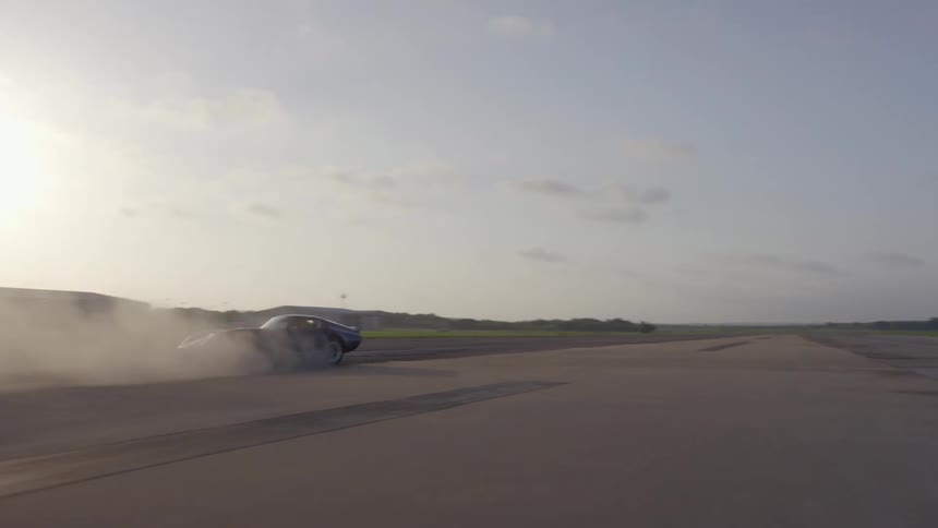 A speeding sports car spins repeatedly on a runway in a grassland during the day