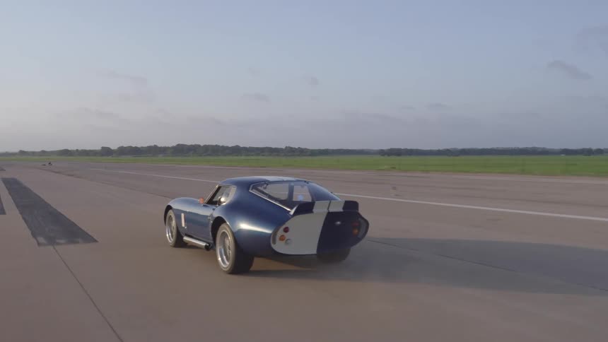 A blue vintage sports car speeds down a straight track