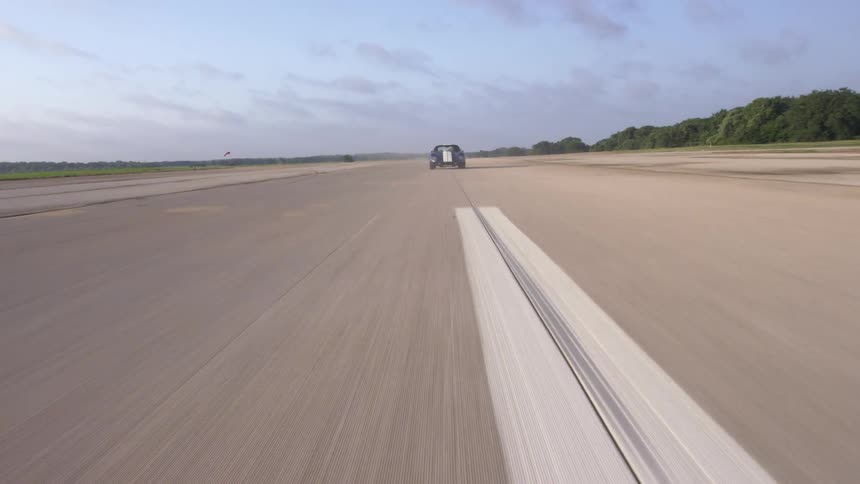 A blue vintage car with white stripes speeds down a rural highway