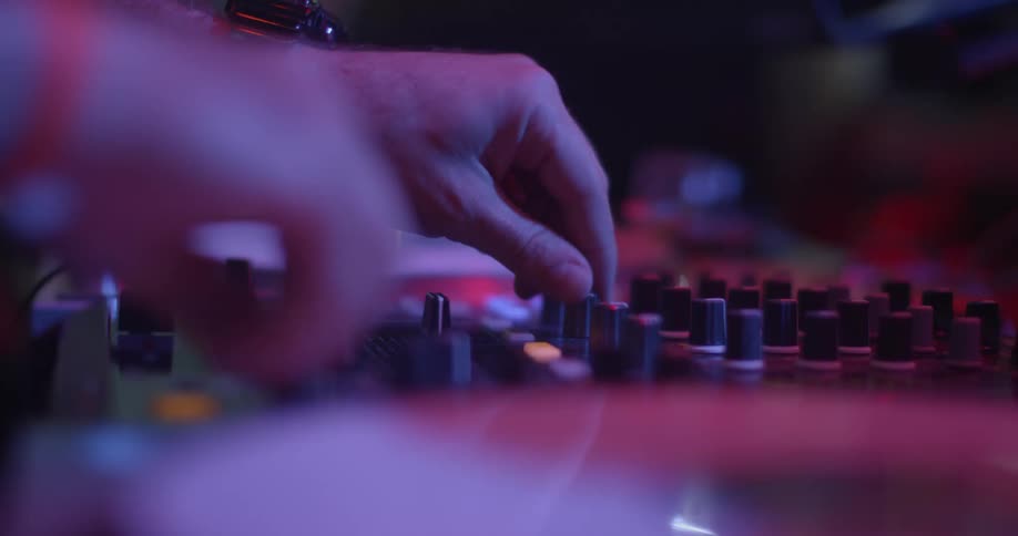 A disc jockey rapidly turns knobs on a control panel as he plays in a night club