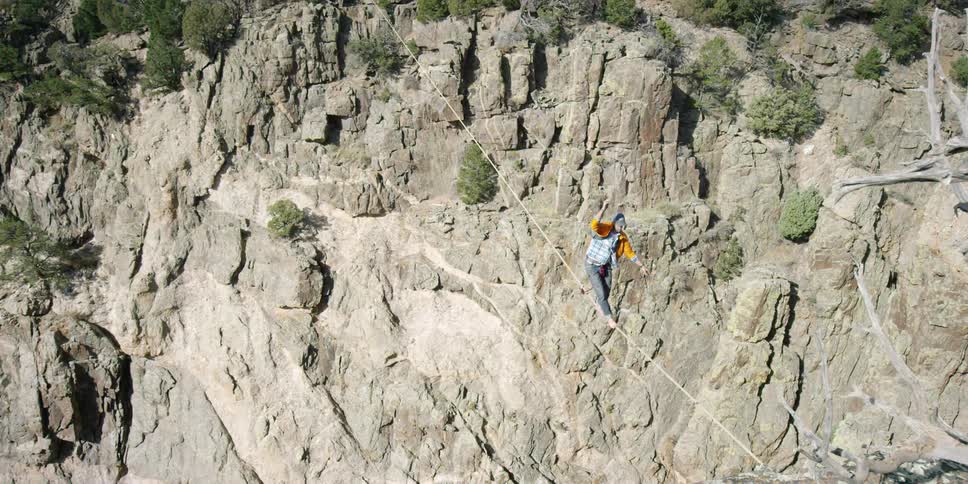 A man carefully balances and walks on a rope strung over a gorge