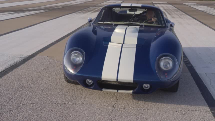 A man sits motionlessly in a sports car parked on a runway in a grassland