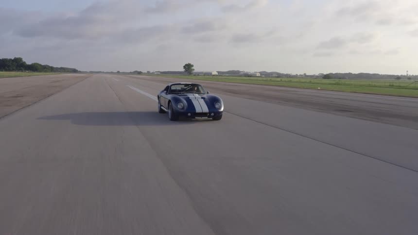 A blue sports car with a white stripe down the middle drives on a highway during the day