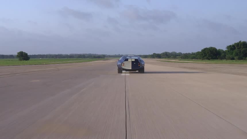 A sports car travels along a wide road through a grassland during the day