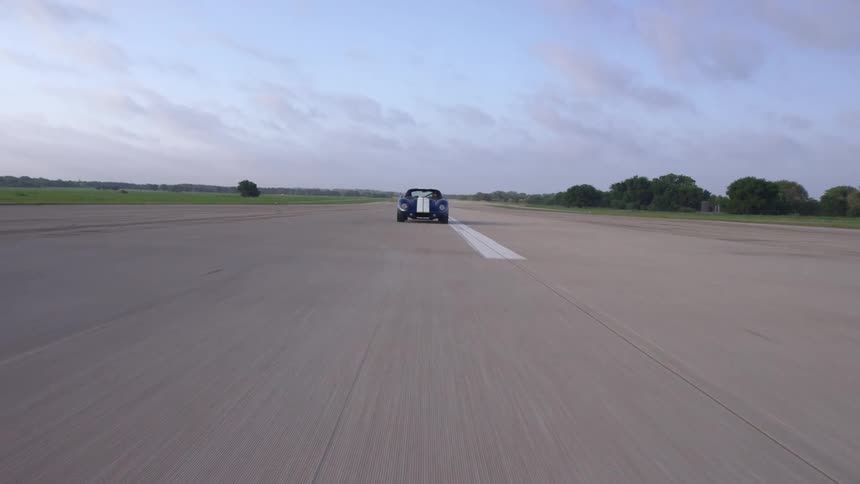 A lone vehicle speeds down a wide road through a flat countryside during the day