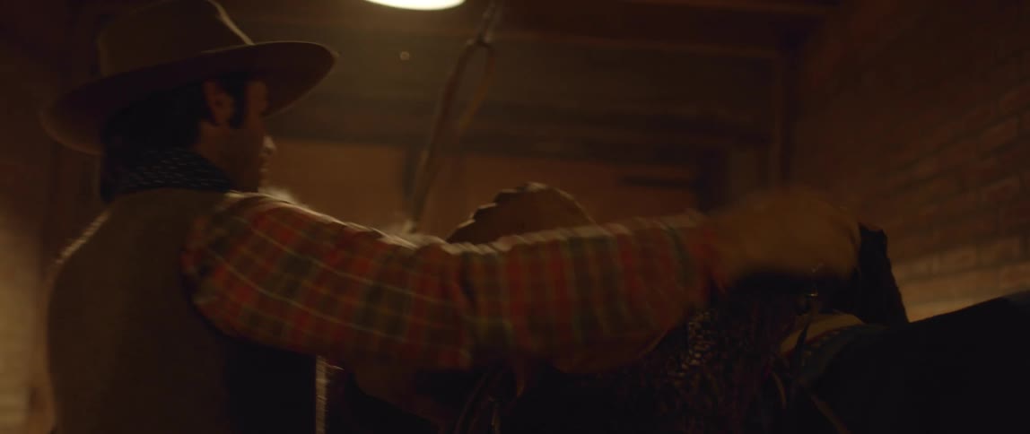 A man places a saddle on a horse in a dark stable