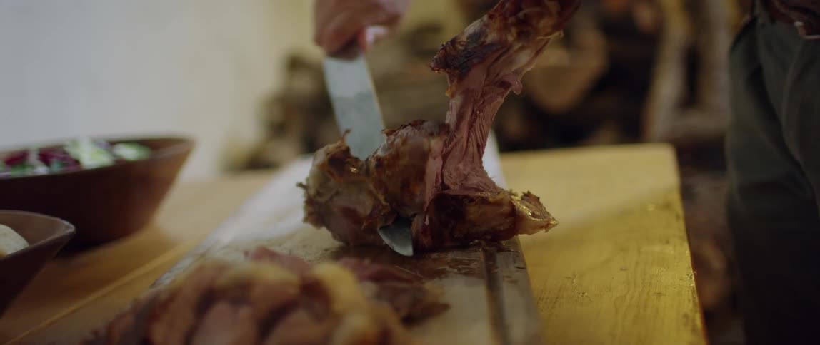 A piece of meat being cut with a knife on a cutting board on a table inside