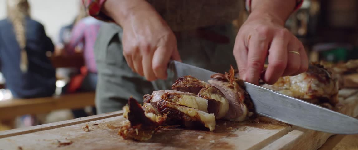 A man cuts a large piece of meat as people sit at a table