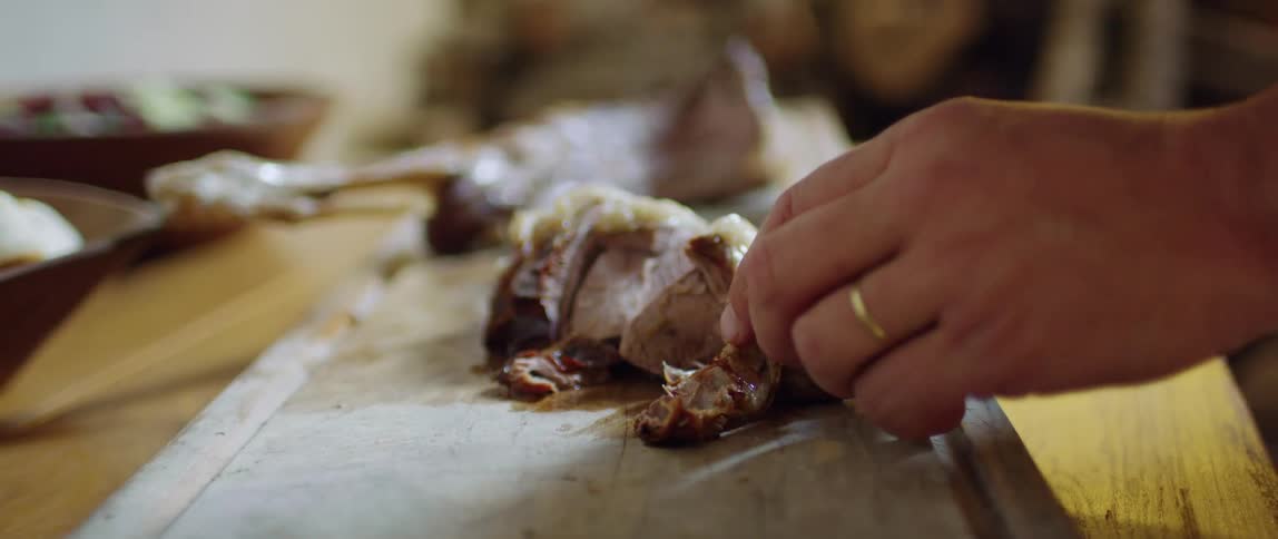 A person uses a knife to cut portions of a meat on a cutting board