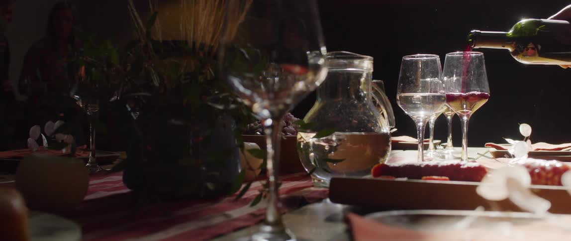 A waiter pours red wine into a glass on a tabletop