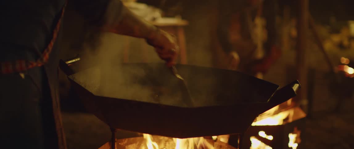 Person cooks on a fire at night while someone else watches from a distance