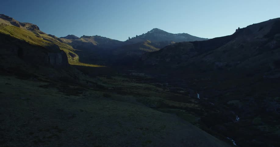 A verdant mountain valley with a narrow stream running along the bottom on a sunny day