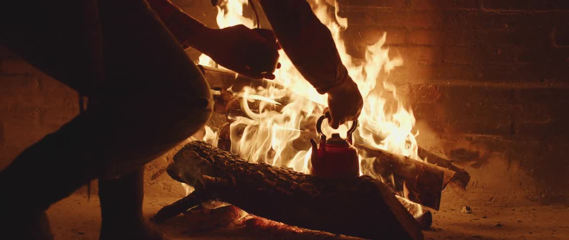 A person heating tea on an indoor fire in a brick fireplace