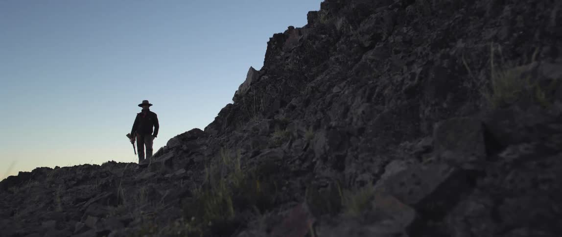 A silhouetted cowboy standing on a mountainside
