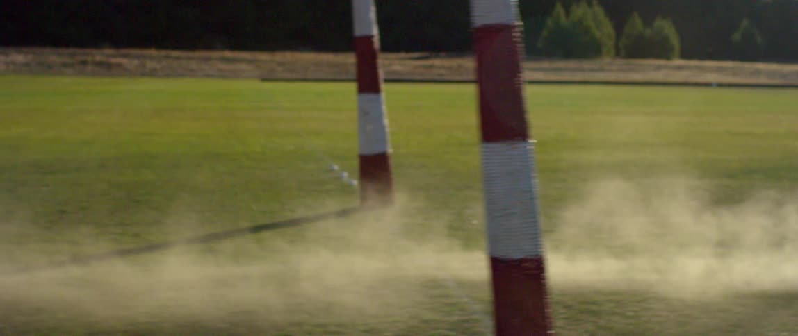 Dust cloud crossing goal posts in a green field at day