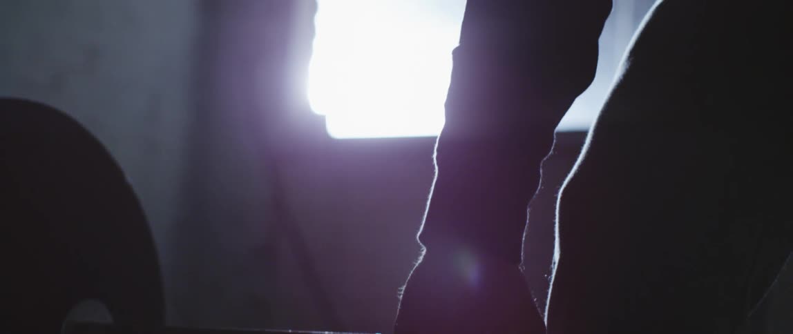 Man lifting up a barbell is silhouetted against the sunlight in the gym