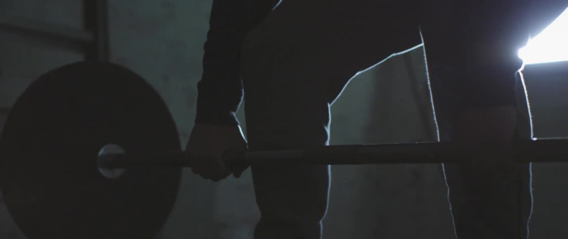 Man lifting up a barbell is silhouetted against the window in the gym