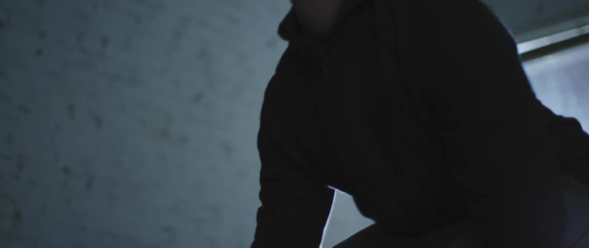 A man in a sweatsuit lifts a barbell in a dimly lit room during the day