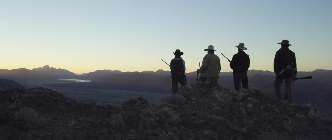 Four men hold rifles and look out over the landscape