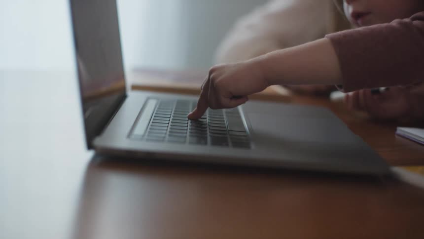 A child presses keys on a laptop keyboard next to an adult