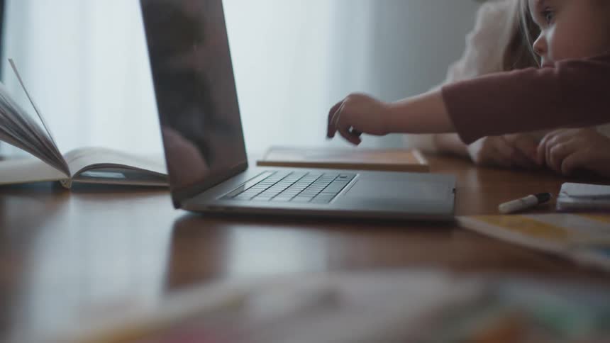 Small girl doing homework at home pressing a key in a laptop over a table