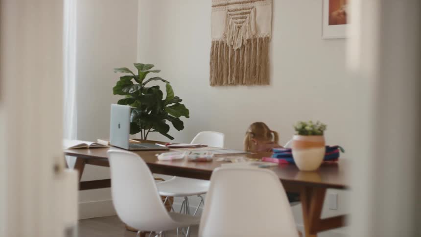 Female child running around dining room table climbs up into a chair and touches the track pad on the laptop that is sitting on the table twice