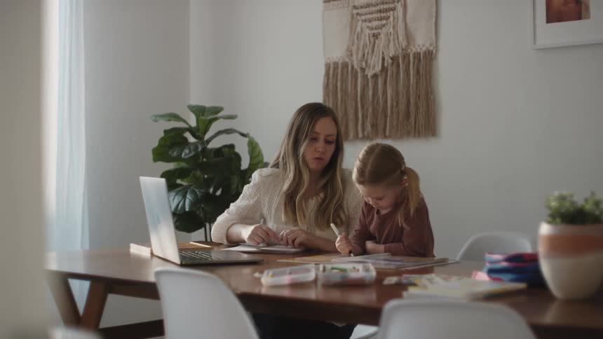 Mother sitting at the table helping daughter with homework at home