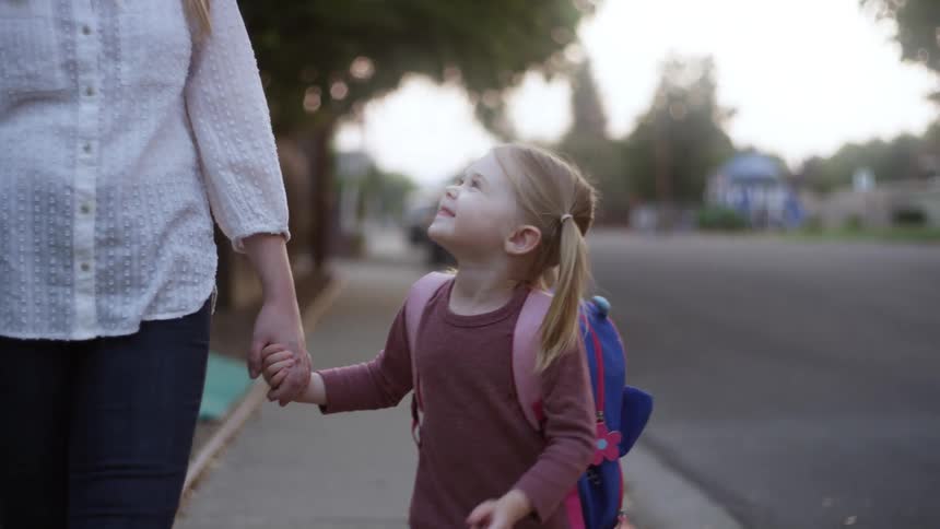 Mother with a white shirt and jeans holds the hand of her daughter and walks down the street