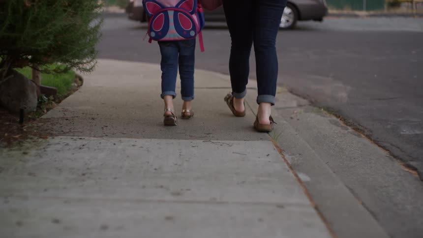 A child walks on a sidewalk with a person in a neighborhood during the day