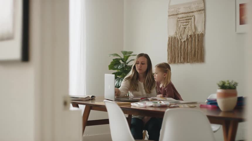 Mother helps daughter study at the table by using a laptop in a room