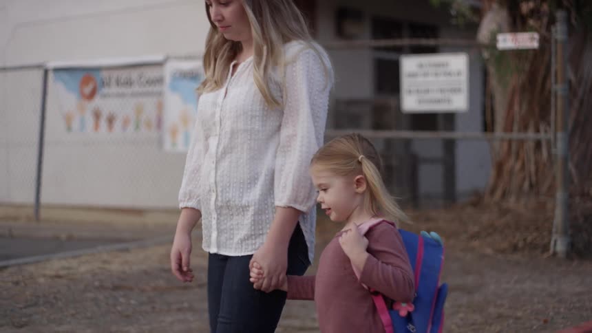 A mom holds her young daughters hand as they walk down a street during the day