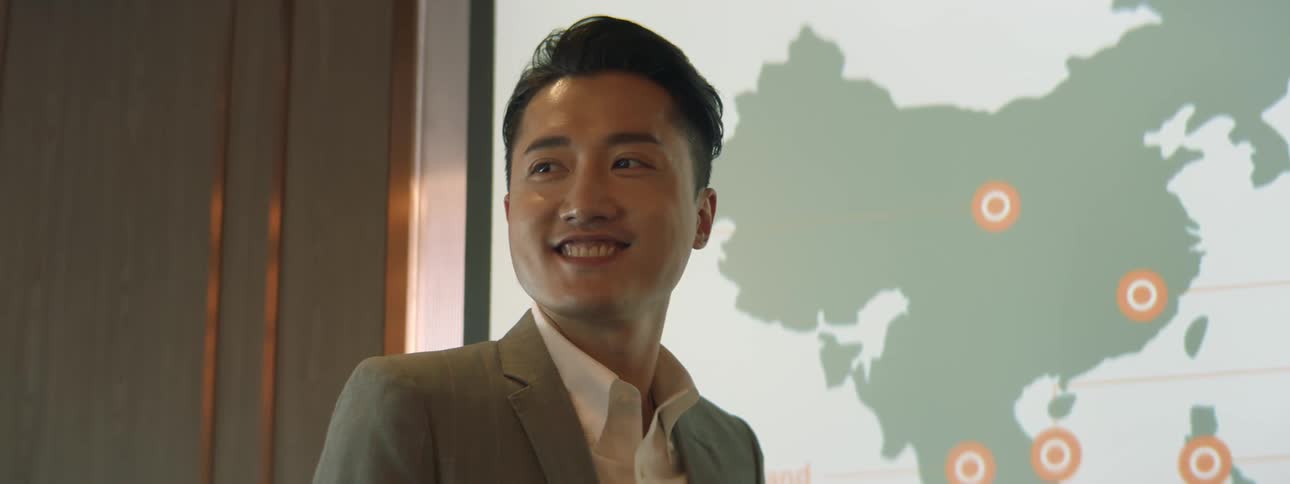 A man in an office stands in front of a large screen and gives a presentation