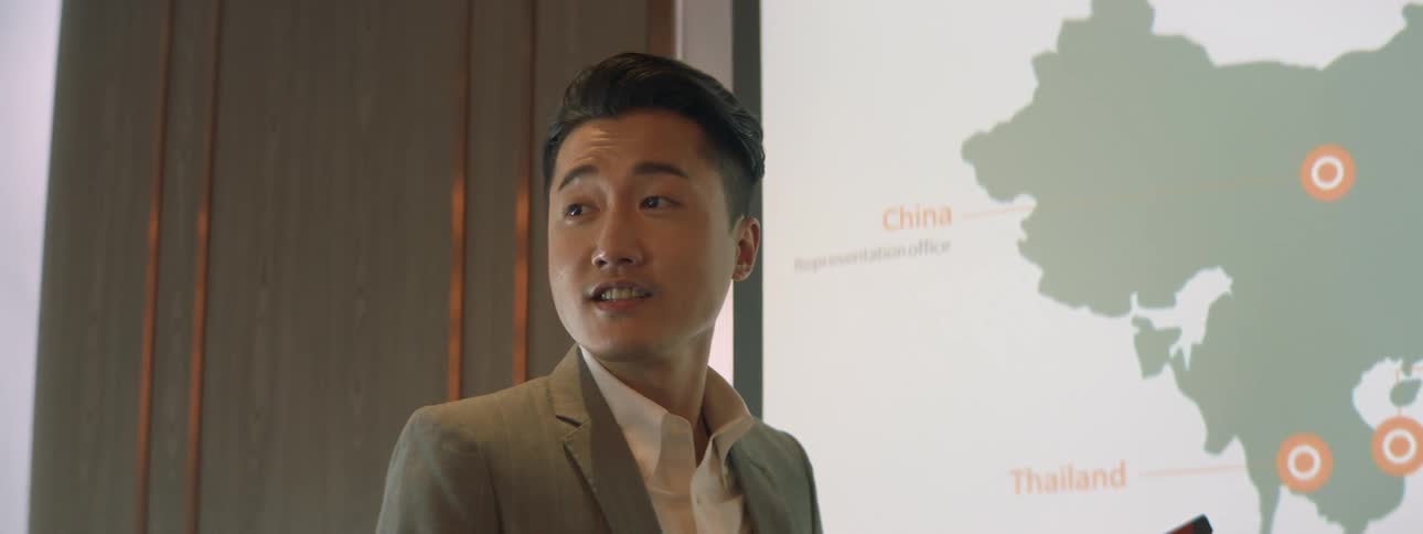 Man in a suit talks while point to a map of asia